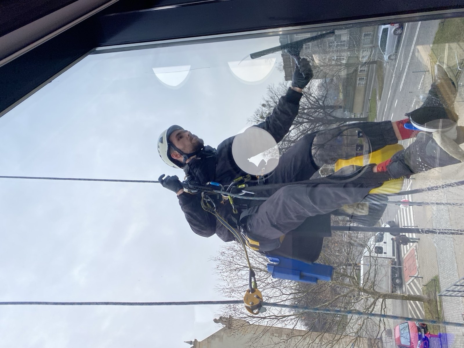 Alpinista przemysłowy w kasku myjący szybę z dostępu linowego