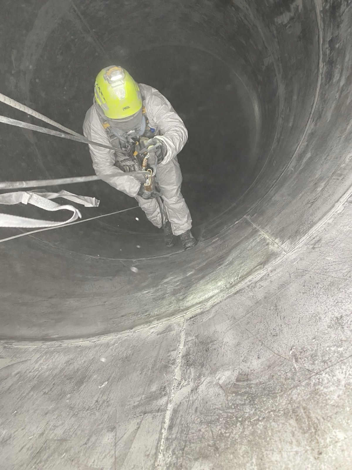 Pracownik w kombinezonie ochronnym czyszczący wnętrze betonowego zbiornika w asekuracji linowej